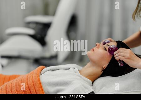 Eine Frau entspannt sich während einer Gesichtsbehandlung mit Rollenwerkzeugen im Spa Stockfoto