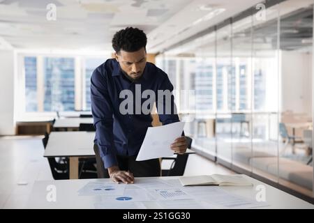 Fokussierter, interessierter junger afrikanischer professioneller Mann, der den Marketingbericht überprüft Stockfoto