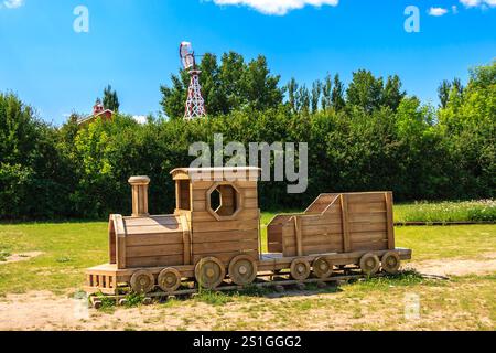 Ein hölzerner Zug sitzt auf einem Feld mit einer großen Windmühle im Hintergrund. Der Zug ist ein kleines Modell und er ist ein Spielzeug. Die Szene ist friedlich Stockfoto