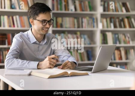 Ein lächelnder junger Mann benutzt das Notizbuch in der Bibliothek für Fernunterricht Stockfoto
