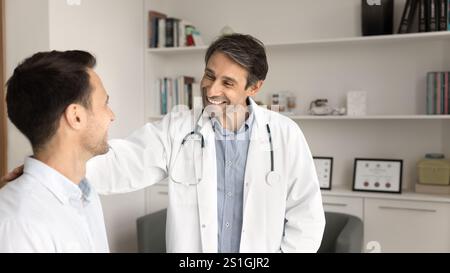 Positiver erfolgreicher männlicher Lateinarzt, der Patienten die Schulter berührt Stockfoto