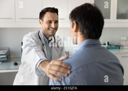 Fröhlicher männlicher Arzt, der die Schulter des Patienten berührt Stockfoto