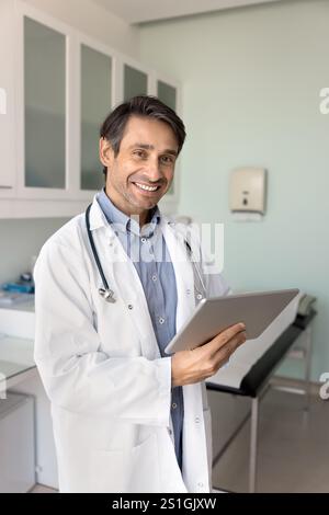 Fröhlicher hispanischer männlicher Arzt, der elektronische medizinische Berichte auf Tablette analysiert Stockfoto