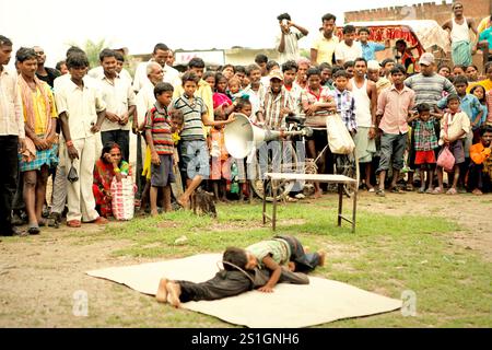 Kinder, die vor Dutzenden von Zuschauern auf einem Feld am Straßenrand am Stadtrand von Rajgir in Bihar, Indien, einen Gymnastikstunt durchführen. Stockfoto