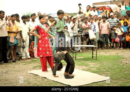 Kinder, die vor Dutzenden von Zuschauern auf einem Feld am Straßenrand am Stadtrand von Rajgir in Bihar, Indien, einen Gymnastikstunt durchführen. Stockfoto