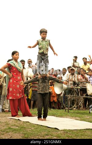 Kinder, die vor Dutzenden von Zuschauern auf einem Feld am Straßenrand am Stadtrand von Rajgir in Bihar, Indien, einen Gymnastikstunt durchführen. Stockfoto