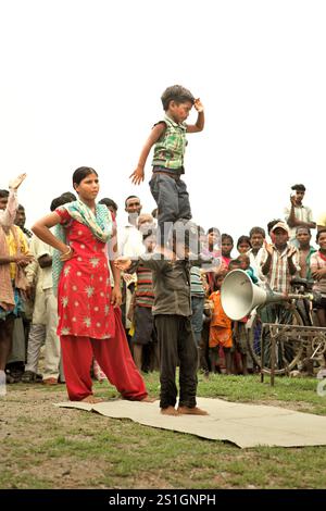 Kinder, die vor Dutzenden von Zuschauern auf einem Feld am Straßenrand am Stadtrand von Rajgir in Bihar, Indien, einen Gymnastikstunt durchführen. Stockfoto