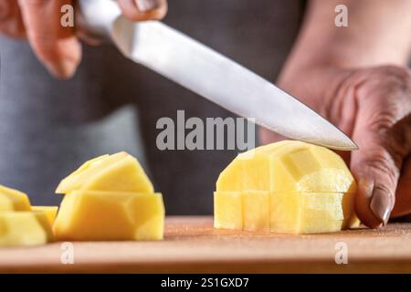 Küchenchef schneidet von Hand frische Kartoffeln zum Kochen auf einem Tisch. Kochen Von Kartoffeln. Koch schneidet rohe Kartoffeln mit einem Messer in kleine Stücke. Kochmann, Herd. C Stockfoto