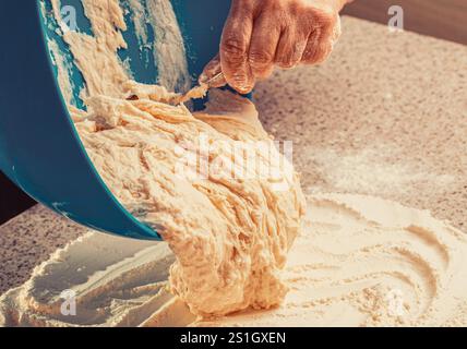 Frau, die Teig mit Hefeteig kneten. Handfrau gießt Teig aus einer Schüssel auf den Tisch Stockfoto