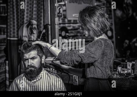 Kunde während der Bartrasur im Friseursalon. Friseurin im Salon. Frau im männlichen Beruf. Friseur schneidet Haare mit Haarschneider. Master bietet Stockfoto