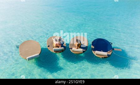 Zwei Freunde genießen einen ruhigen Tag auf schwimmenden Liegen unter der hellen Sonne im klaren türkisfarbenen Wasser von Koh Kood. Die ruhige Atmosphäre lädt zu einem Besuch ein Stockfoto