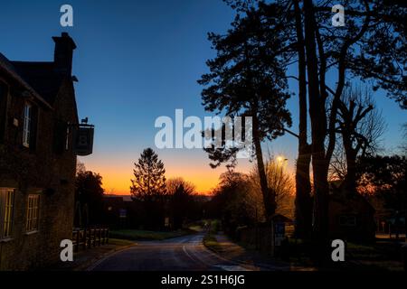 Kiefern und die Silhouette des Bell Pubs in der Farbe des Winters. Wold, Cotswolds, Gloucestershire, England Stockfoto