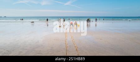 Ein Panoramabild von zwei RNLI-Rettungsschwimmern, die in Stühlen sitzen und bei Ebbe Urlauber im Meer am GT Great Western Beach in Newquay beobachten Stockfoto