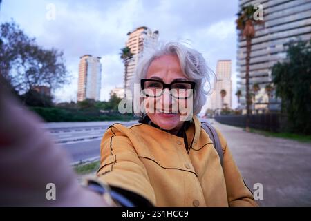 Seniorin macht Selfie in der Stadt, während sie lächelt und ihr Handy hält. Stockfoto