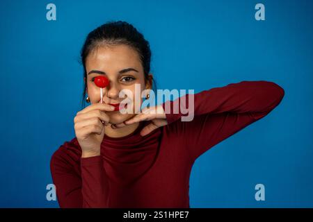 Studio-Porträt einer fröhlichen jungen Frau, die ein Auge mit einem Lutscher bedeckt und Freude und Verspieltheit ausdrückt Stockfoto