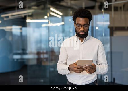 Ernsthafter Geschäftsmann mit Tablet-Computer in der Hand. Junger Mann in Geschäftskleidung mit App, liest E-Mails und sieht Finanzdaten online an. Stockfoto