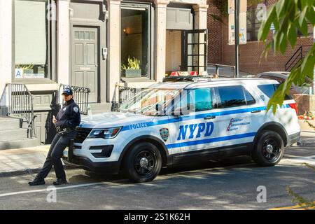 Weiblicher NYPD-Offizier lehnt sich gegen die Kapuze eines Patrouillenkreuzers, der an einem sonnigen Tag auf der Front Street in Brooklyn, New York City, geparkt hat Stockfoto