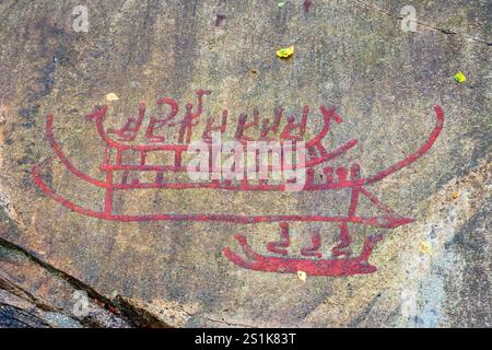 Die Gesteinsschnitzereien des Tanum auf dem Vitlycke-Flachfelsen, rot bemalt, zeigen Menschen auf Booten aus der Bronze- und Eisenzeit. Stockfoto
