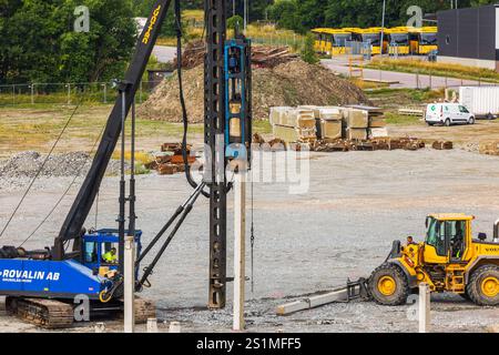 Baustelle mit schweren Maschinen, die auf Fundamentstapeln arbeiten und von Baumaterialien umgeben sind. Stockfoto