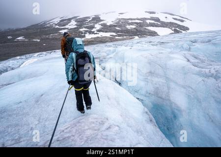 Zwei Personen laufen in der Nähe einer großen Spalte am Austdalsbreen-Gletscher in Jostedal, Norwegen. Sie sind zusammengeschnürt und mit der notwendigen gea ausgestattet Stockfoto