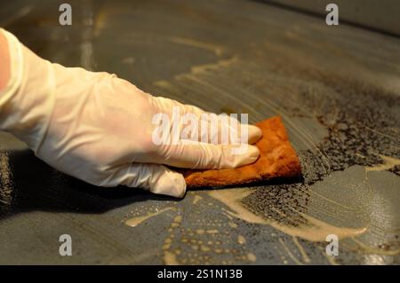 Die Hand einer Frau in einem Latex-Schutzhandschuh wäscht einen schmutzigen Ofen mit einem Schwamm. Der Schwamm ist gerissen. Starke Verschmutzung. Stockfoto