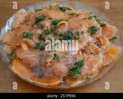 Dünn geschnittene Gravlax, geräucherter Lachs mit Dill, ist elegant auf einer Glasplatte angeordnet und servierfertig. Stockfoto