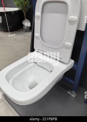 Eine elegante, moderne Toilette steht in einer Ausstellung mit innovativen Badezimmerarmaturen im Vordergrund. Die glänzende weiße Keramik steht im Kontrast zum min Stockfoto