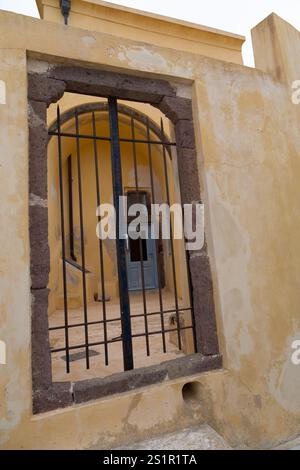 Schmiedeeisernes Tor, das zu einem alten Gebäude mit einer strukturierten gelben Mauer führt, Santorin, Griechenland Stockfoto