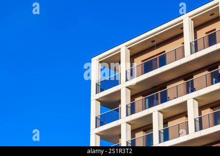 Ein modernes Wohngebäude mit Balkonen steht vor einem hellblauen Himmel und zeigt sein elegantes Design und seine Struktur. Stockfoto