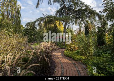 Ein geschwungener Backsteinweg führt durch einen gepflegten Garten mit üppiger Vegetation und blühenden Blumen, Kreislehrgarten Steinfurt, Burgsteinfurt, Münsterla Stockfoto