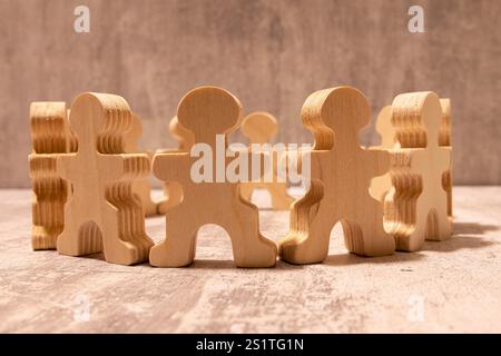 Viele verschiedene Papiermenschen stehen im Kreis auf einem Holztisch vor beigefarbenem Hintergrund. Diversitäts- und Integrationskonzept Stockfoto