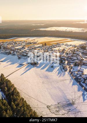Luftaufnahme eines schneebedeckten Dorfes neben einem dichten Wald im sanften Licht des späten Nachmittags, Simmersfeld, Bezirk Calw, Schwarzwald, Deutschland, E Stockfoto