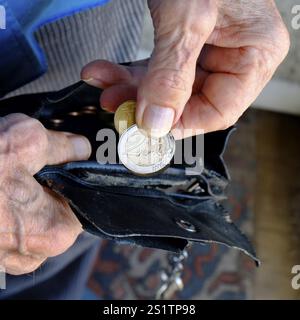 Armut: Die Finger einer Seniorin nehmen zwei Euro-Münzen aus einer verschlissenen Geldbörse. Quadratisches Format. Armut: Die Finger eines Seniors nehmen zwei Euro-Münzen Stockfoto