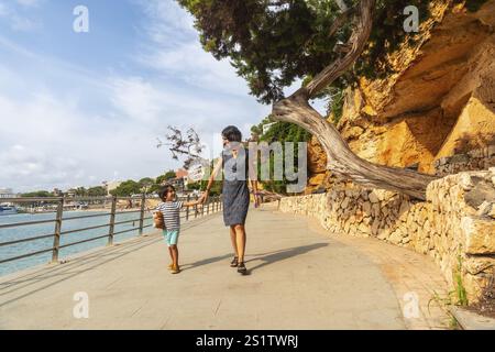 Mutter und Sohn genießen ihren Urlaub bei einem Spaziergang entlang der Strandpromenade in porto cristo, einer bezaubernden Küstenstadt in manacor, mallorca, spanien Stockfoto