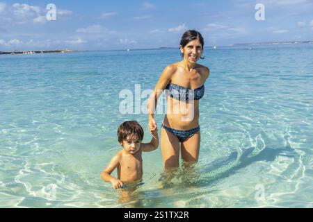 Eine Frau und ein Kind sind im Meer. Die Frau hält die Hand des Kindes. Die Szene ist fröhlich und verspielt Stockfoto