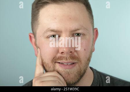 Bärtiger, lässiger junger Mann in einem grauen T-Shirt, der nachdenklich in die Kamera schaut. Ein frontales Studio-Porträt in Nahaufnahme Stockfoto