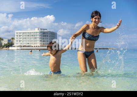 Eine Frau und ein Kind spielen im Meer. Die Frau hält die Hand des Kindes Stockfoto