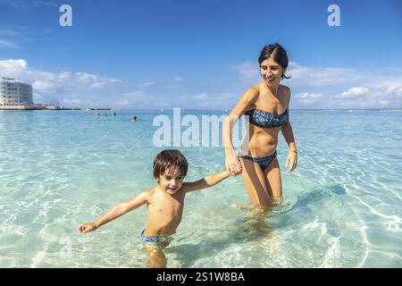 Eine Frau und ein Kind spielen im Meer. Die Frau hält die Hand des Kindes Stockfoto