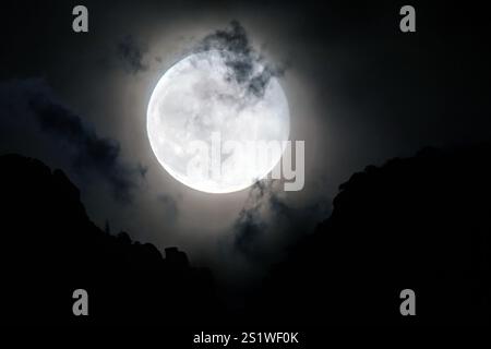 Vollmond, der über Berge mit fleckigen Wolken aufsteigt Stockfoto