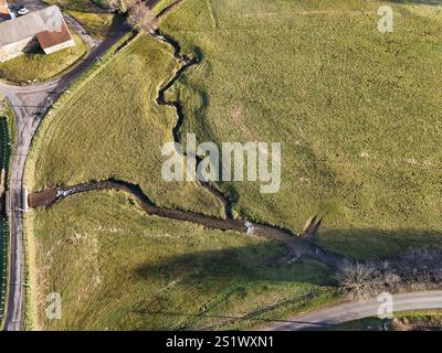 Aus der Vogelperspektive eines kleinen sich windenden Flusses durch grasbewachsene Felder in Burgund, Frankreich Stockfoto