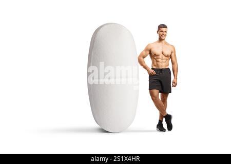 Porträt eines Bodybuilders in voller Länge, der neben einer großen Pille steht, isoliert auf weißem Hintergrund Stockfoto