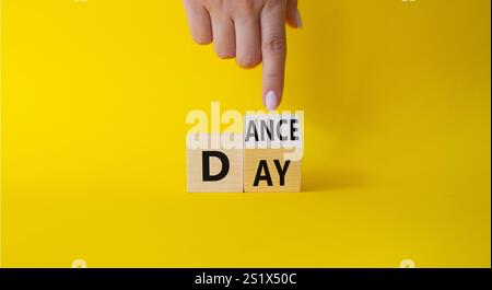 Symbol für den Internationalen Tanztag. Die Hand des Geschäftsmannes zeigt auf gedrehte Holzwürfel mit den Worten Dance Day. Schöner gelber Hintergrund. Internationaler Tanz Stockfoto