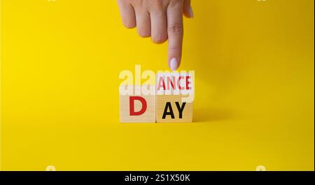 Symbol für den Internationalen Tanztag. Die Hand des Geschäftsmannes zeigt auf gedrehte Holzwürfel mit den Worten Dance Day. Schöner gelber Hintergrund. Internationaler Tanz Stockfoto