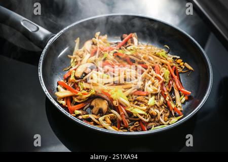 In einer schwarzen Pfanne frittiertes Gemüse, wie Pilze, rote Paprika, Sojasprossen und Kohl, zum Kochen einer asiatischen Mahlzeit, ausgewählt für Fo Stockfoto