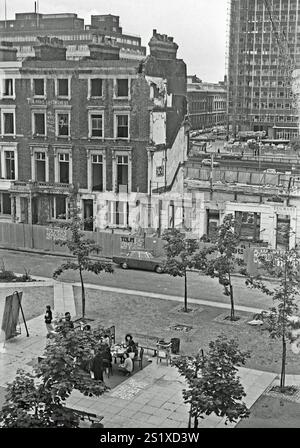 Blick auf Tolmers Square, Somers Town, London, England, Großbritannien, während der Proteste in den späten 1970er Jahren Die Bewohner sitzen auf dem Platz, und auf den Gebäuden sind handgemalte Slogans zu sehen, die teilweise fast abgerissen wurden, sowie Wellblechzäune. Der Tolmers Square befindet sich in Somers Town in der Nähe des Bahnhofs Euston im Zentrum Londons und wurde in den 1970er Jahren von mehr als hundert Hausbesetzern besetzt, die zusammen mit lokalen Gruppen für einen Sanierungsplan kämpften, der der lokalen Gemeinde entsprach. Bis 1975 hatte das „Tolmers Village“ 49 Besatzungen, in denen mehr als 180 Menschen untergebracht waren. Die Hausbesetzer lebten dort sechs Jahre. Stockfoto