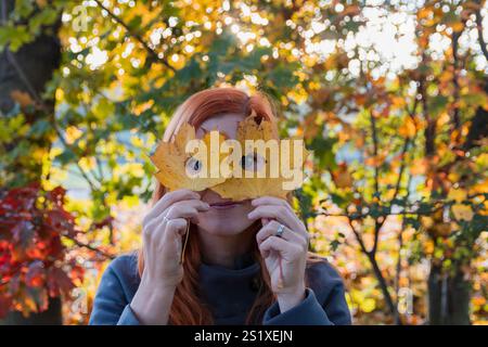 Junge rothaarige schöne Frau, die Herbstblatt hält. Lebensstil, gesichtsloser Hintergrund Stockfoto