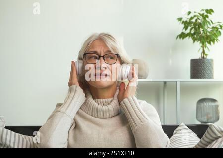 Seniorin genießt ein Hörbuch in einer entspannten häuslichen Umgebung Stockfoto