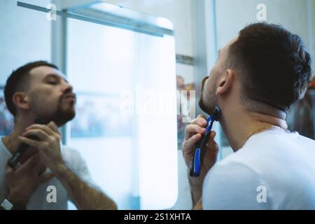 Der Kerl rasiert sich vor einem Spiegel Stockfoto
