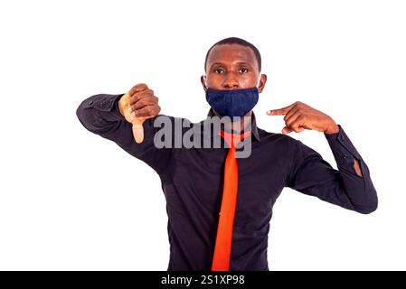 Porträt des jungen Geschäftsmannes, der mit Daumen nach unten zeigt und Stoffmaske mit Zeigefinger zeigt. Stockfoto