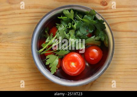 Frisches Gemüse wird in der Metallschale gewaschen, die mit kaltem Wasser gefüllt ist, auf dem Vintage-Schneidebrett aus zerrissenem Holz. Bio-Tomaten, Petersilie, ce Stockfoto